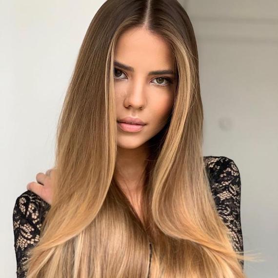 Photo of woman with caramel blonde balayage through straight hair, created using Wella Professionals. 