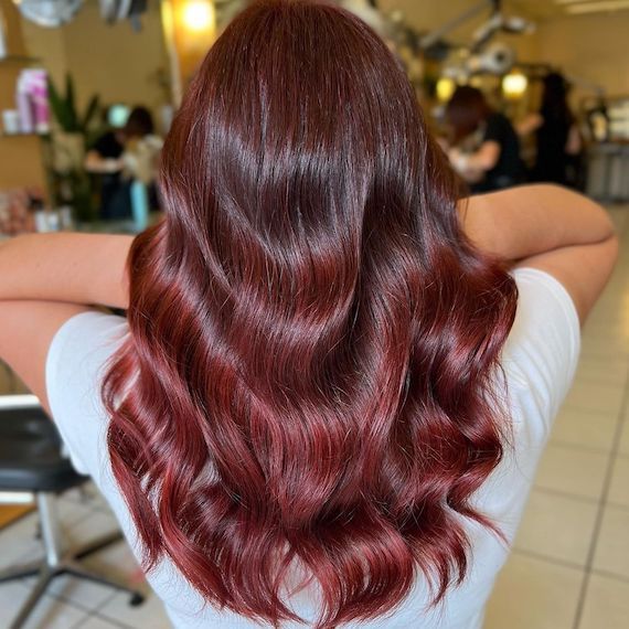 Back of model’s head with long, wavy, burgundy red ombre hair.