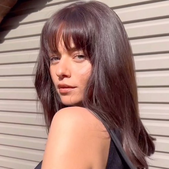Model with long, shiny, dark brown hair and classic bangs.