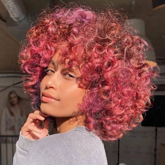 Model with shoulder-length, fuchsia pink, curly hair and tapered bangs.