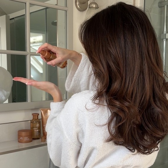 Model with long, brown hair pumps ULTIMATE SMOOTH Miracle Oil Serum into hand.