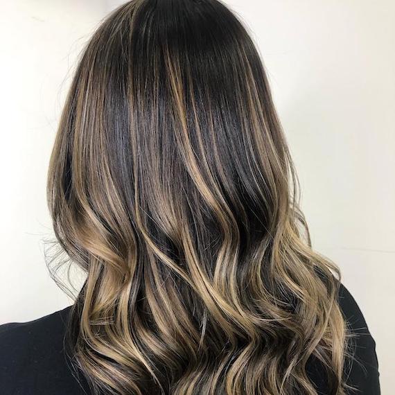 Back of woman’s head with loosely curled, dark brown hair and golden blonde highlights, created using Wella Professionals.