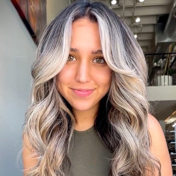 Model with a black root shadow and silver blonde balayage styled in loose waves.