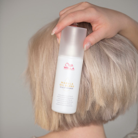 Back of woman’s head as she holds Wella Marula Oil Blend Scalp Primer in front of her blonde bob.