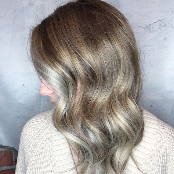 Side profile of woman with long, wavy hair and ash blonde balayage, created using Wella Professionals.