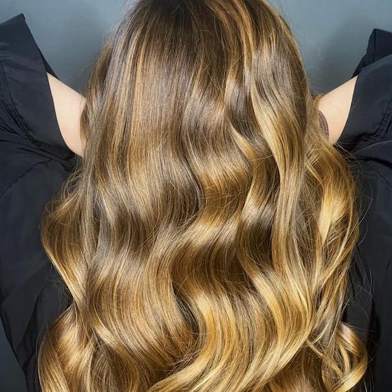 Back of woman’s head with long, loosely-curled hair and dirty blonde balayage, created using Wella Professionals.