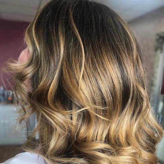 Back of woman’s head with blonde balayage on wavy, brown hair, created using Wella Professionals.