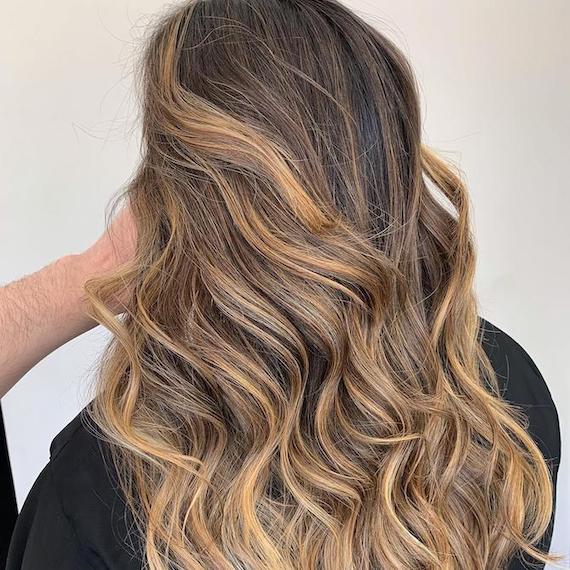 Back of woman’s head with light brown balayage through wavy hair, created using Wella Professionals.