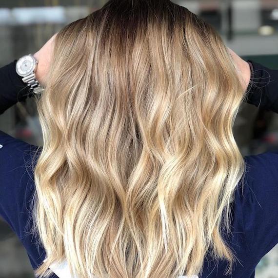 Blonde balayage on long, wavy hair, created using Wella Professionals.