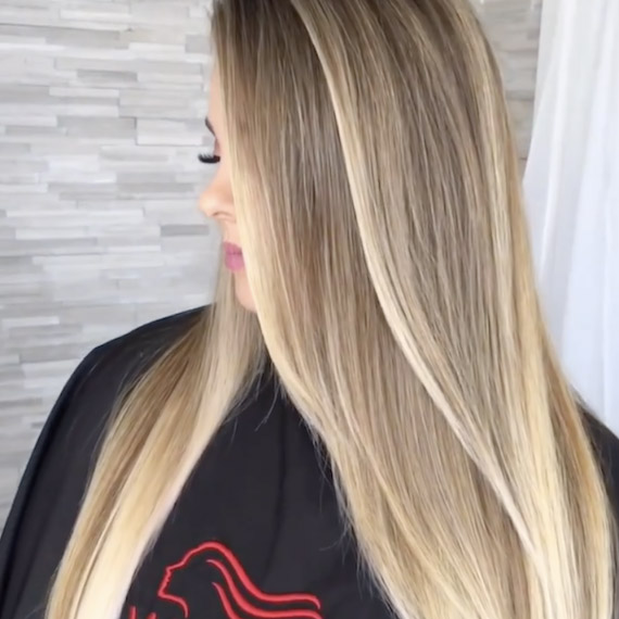 Profile of a person with long honey blonde ombre hair wearing a Wella Professionals salon cape
