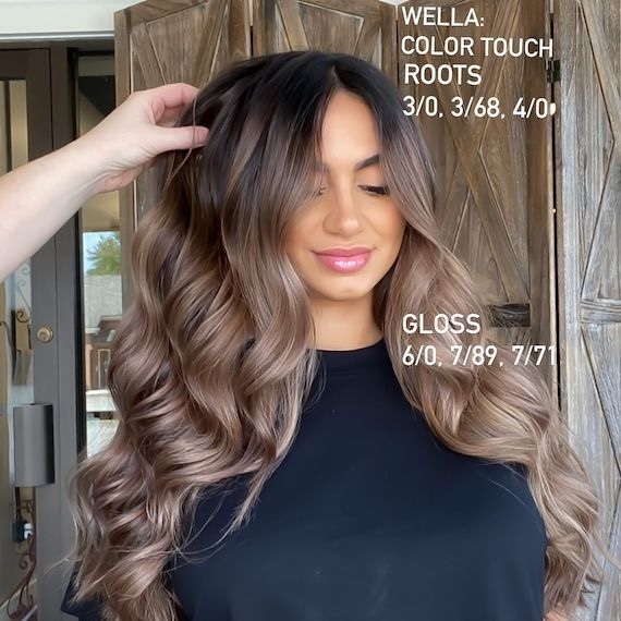 Model with a brown root shadow and mushroom blonde balayage through loosely curled hair.