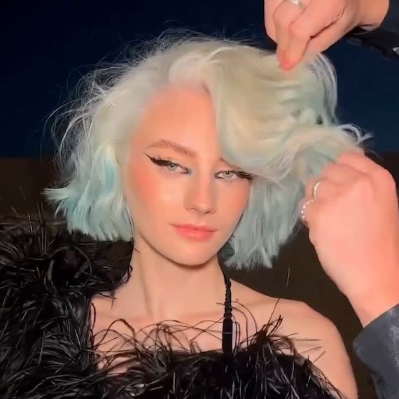 Model with a platinum blonde and blue ombre, wavy bob faces the camera.