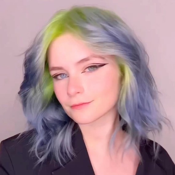Model will choppy, mid-length, blue and green ombre hair faces the camera.