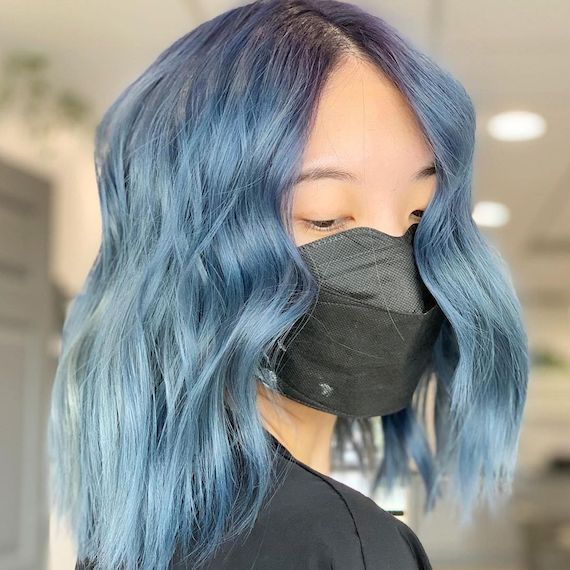 Model with mid-length, wavy, denim blue ombre hair glances down while facing the camera.