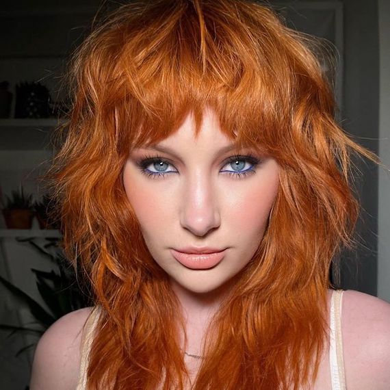  Model with red hair and shag haircut faces camera.
