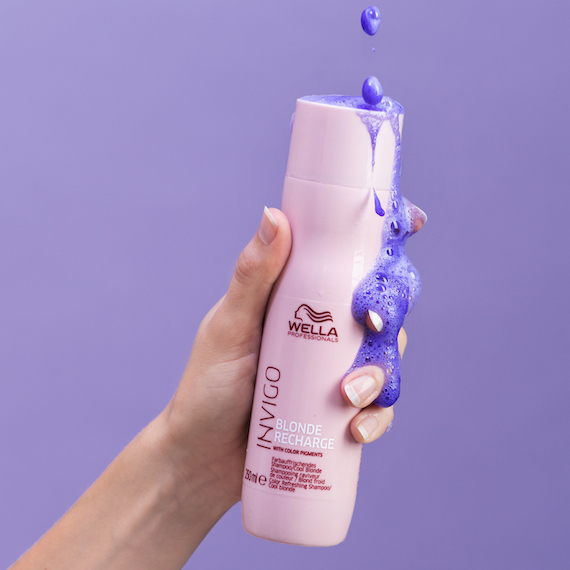 Hand holds Cool Blonde Shampoo. Violet pigment spills down the side of the bottle.