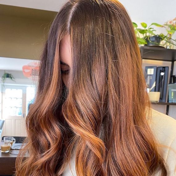 Model glances down to show off light copper brown hair styled in a bouncy blow-dry.