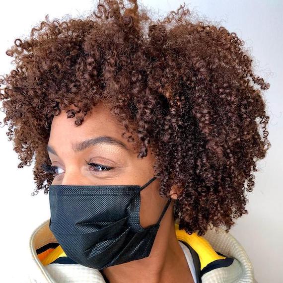 Woman wearing face mask, with curly copper brown hair created using Wella Professionals.