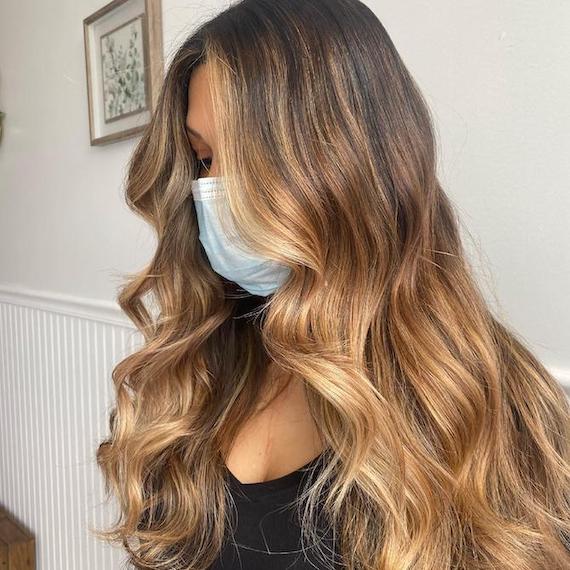 Side profile of woman with long, wavy hair and brown to blonde balayage, created using Wella Professionals.
