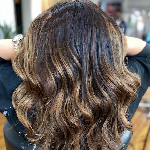 Dark brunette hair with golden highlights styled into loose waves