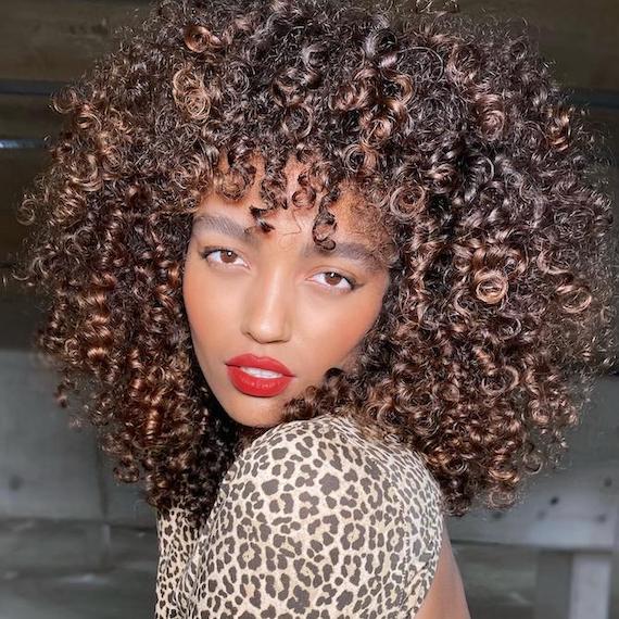 Model with voluminous frosted chestnut brown curly hair wearing red lipstick and a leopard print top