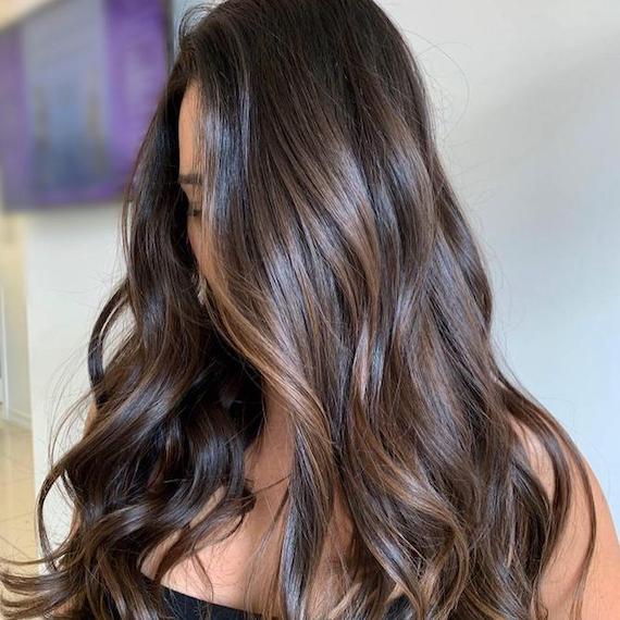 Woman with long, wavy, dark brown hair and balayage, created using Wella Professionals.