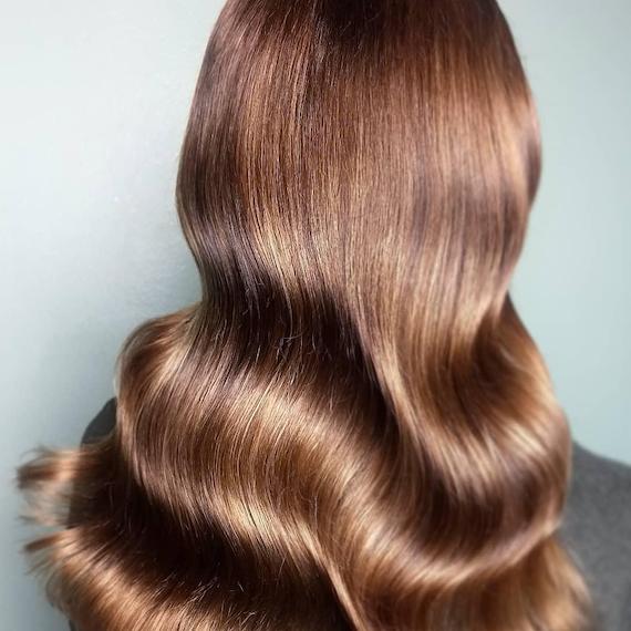 Back of woman’s head with long, wavy, glossy caramel brown hair, created using Wella Professionals. 