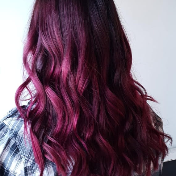 Woman with long, burgundy pink hair styled with loose waves