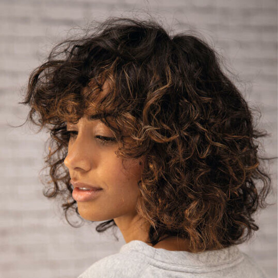 Side profile of woman with golden twilighting through dark curly hair, created using Wella Professionals.