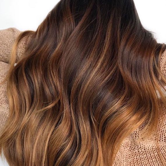 Back of person’s head. They lift their long, wavy, cappuccino colored hair.