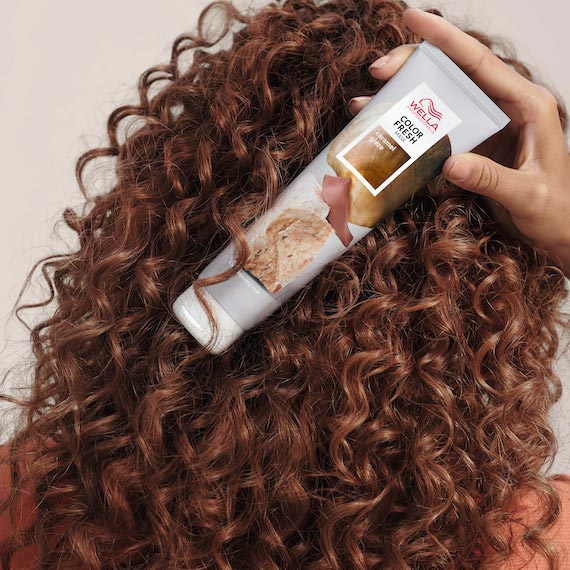 Model holds Color Fresh Mask in Caramel Glaze in front of brown, curly hair.