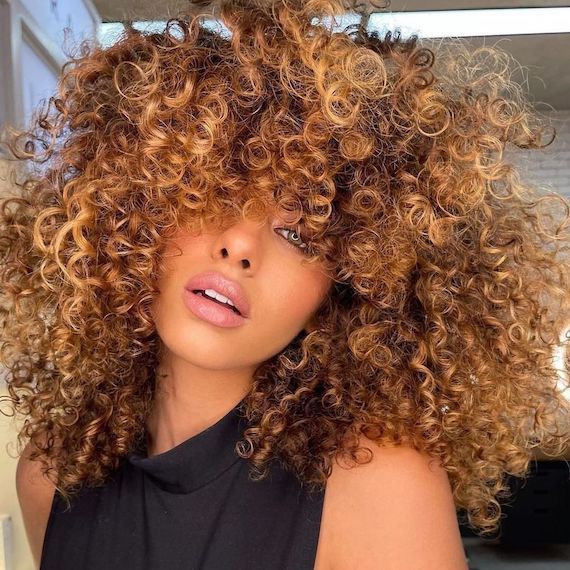 Model with curly, cappuccino coloured hair looks at the camera.