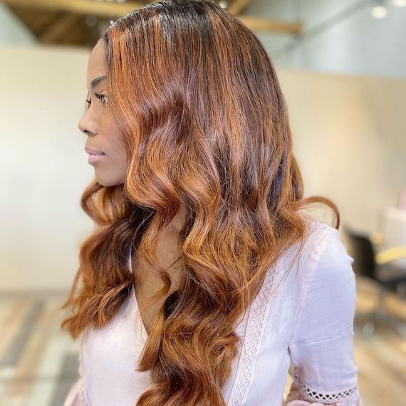 Model looks to the side to reveal their long, wavy hair that’s been colored with cinnamon and cappuccino brown hues. 