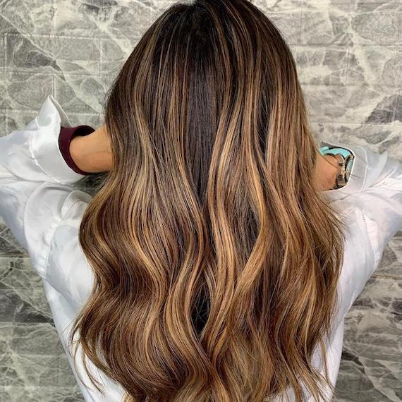 Frau mit gewelltem, mittellangem, braunem Haar und einem kräftigen, karamellfarbenem Balayage, kreiert mit Wella Professionals.