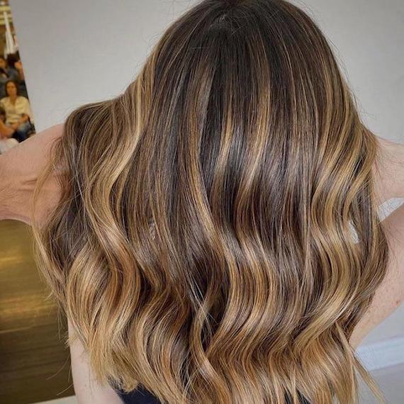 Back of woman’s head with wavy, brown hair and caramel honey blonde balayage, created using Wella Professionals.