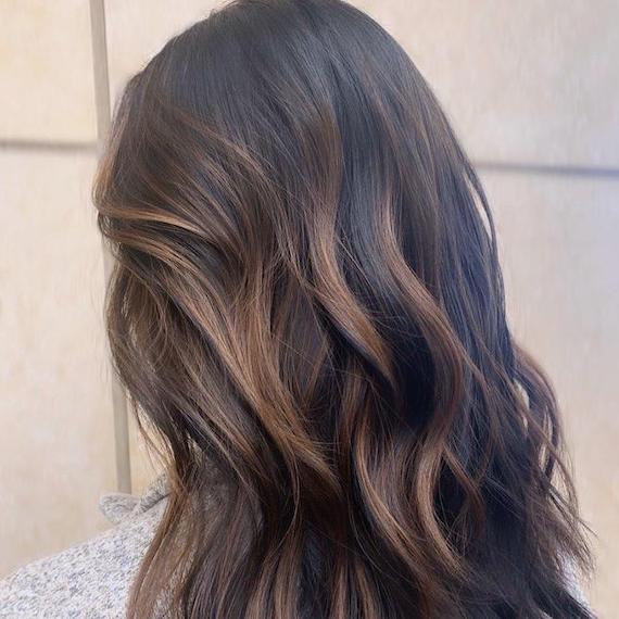 Frau mit dunkelbraunem Haar und einer Karamell-Balayage, kreiert mit Wella Professionals.