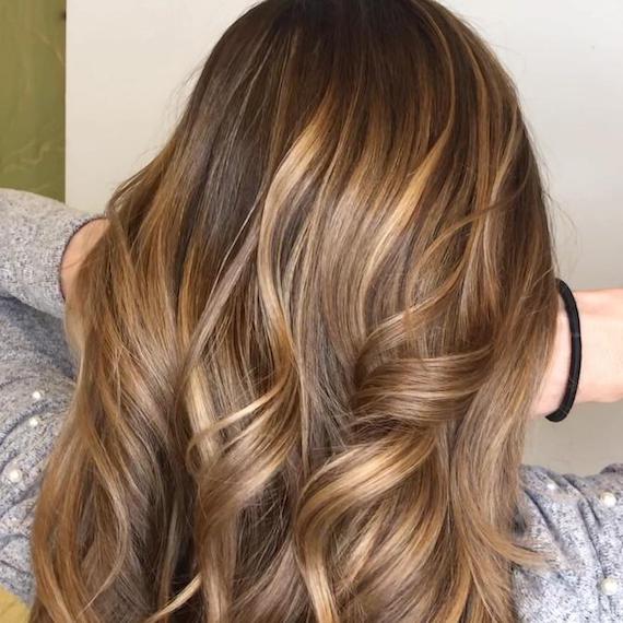 Frau mit braunem Haar und einer hellen karamellblonden Balayage, kreiert mit Wella Professionals.