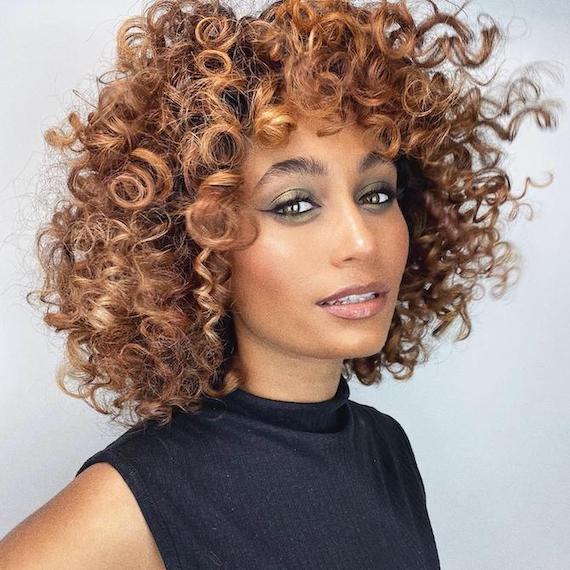 Woman facing the camera with brown, curly hair and caramel balayage, created using Wella Professionals.