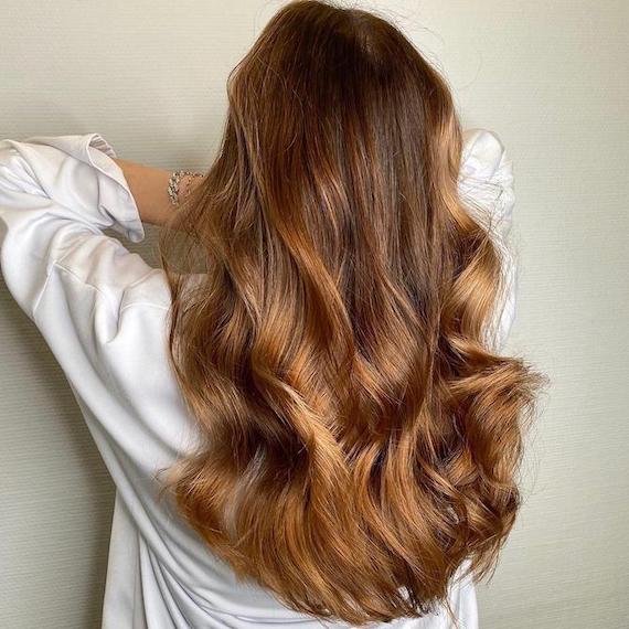 Back of woman’s head with long, loosely curled, brown hair and caramel balayage, created using Wella Professionals.