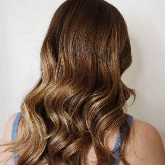 Back of woman’s head with long, loosely curled hair and caramel blonde balayage, created using Wella Professionals.  