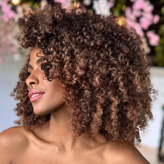 Brunette woman with subtle caramel highlights adding soft dimension to curly hair.