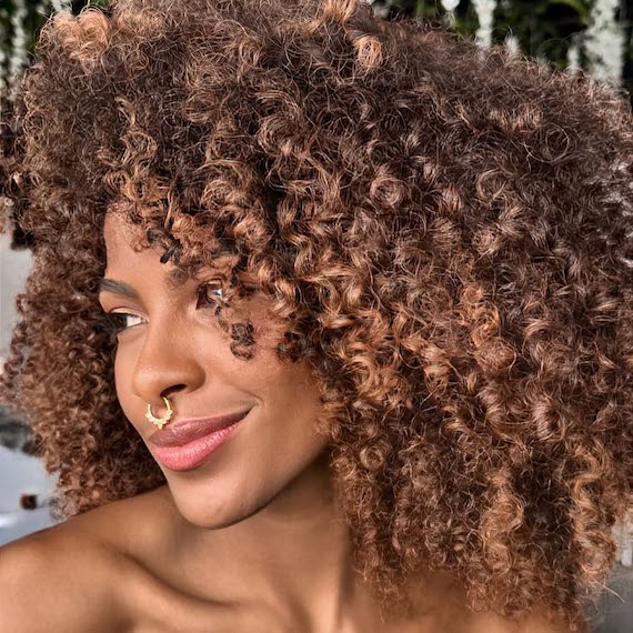 Brunette woman with subtle caramel highlights adding soft dimension to curly hair.