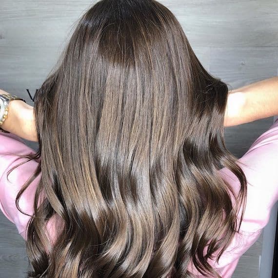 Image of the back of a woman’s head, showing super-shiny brunette hair styled in loose waves.