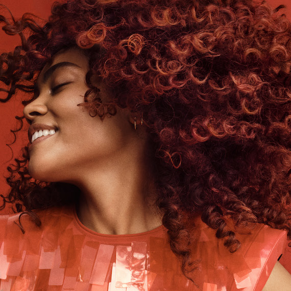 Model smiles while swishing their red-brown, curly hair.