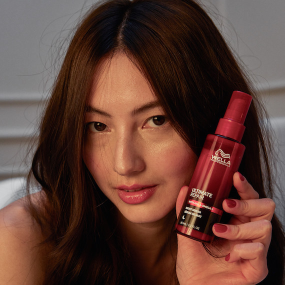 Model with dark brown hair holds up a bottle of ULTIMATE REPAIR Night Serum.