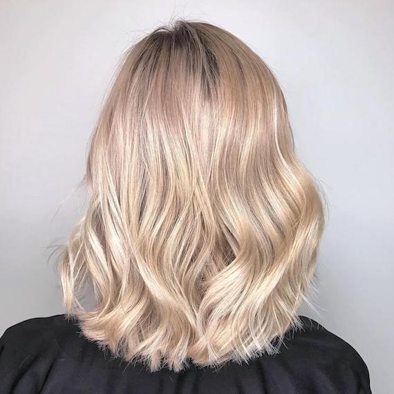 Image of the back of a woman’s bob cut with creamy powdered blonde hair color styled in soft waves.