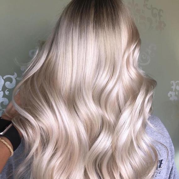 Image of the back of a woman’s head with platinum powdered blonde hair color styled in long, loose waves.