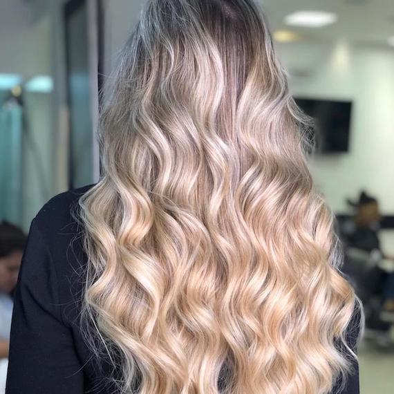 Photo of the back of a woman’s head with warm powdered blonde hair color and long hair styled in tonged curls.