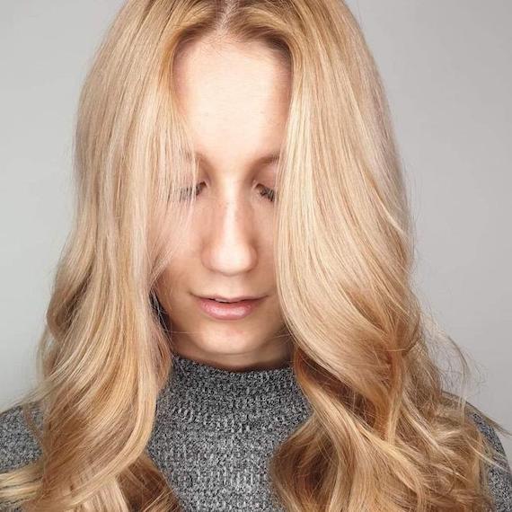 Headshot of a woman with golden powdered blonde hair color, styled in loose, face-framing waves.