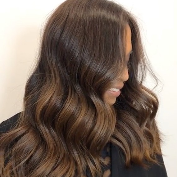 Side profile of a person with long, wavy chocolate brown balayage hair